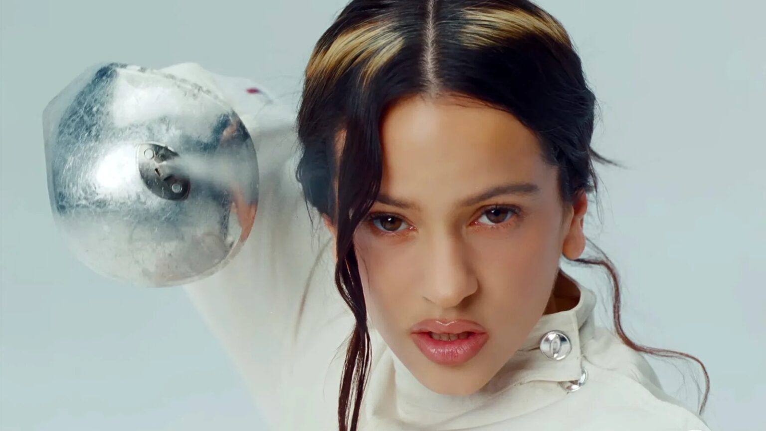 Rosalía en traje de esgrima blanco, protegida contra el desamor, con perros blanco y negro simbolizando caos emocional interno.