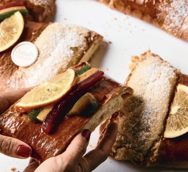 Manos familiares compartiendo rebanada de rosca de Reyes recién cortada, mostrando interior esponjoso con relleno cremoso y frutas cristalizadas
