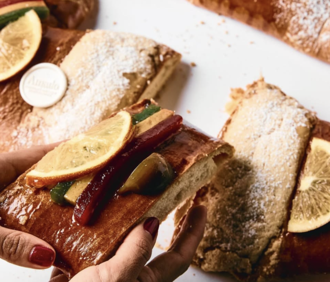 Manos familiares compartiendo rebanada de rosca de Reyes recién cortada, mostrando interior esponjoso con relleno cremoso y frutas cristalizadas