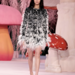 Vestidos de tul alado cascatean desde corsets raso etéreos, mientras tweed esporulado moldea chaquetas vivas con solapas troncos retorcidos.