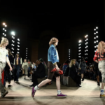 Modelo desfila en la pasarela de Coach NYFW con patchwork blazer entallado volteado mostrando forro estampado vibrante, Kisslock Frame Bag scrunched en cuero glove-tanned bajo el brazo.