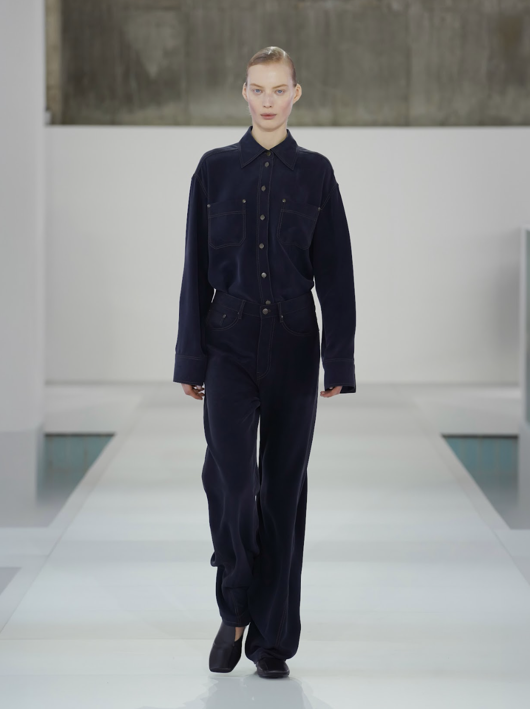 Desfile COS Primavera-Verano 2026 en Seúl: modelos emergen en neblina brutalista con looks en grises y el Monument Tote icónico.