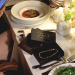 Grupo de invitadas elegantes en negro y nude alrededor de una mesa con velas en la cena de Aleví Milano FW26/27 en Blanco Castelar.