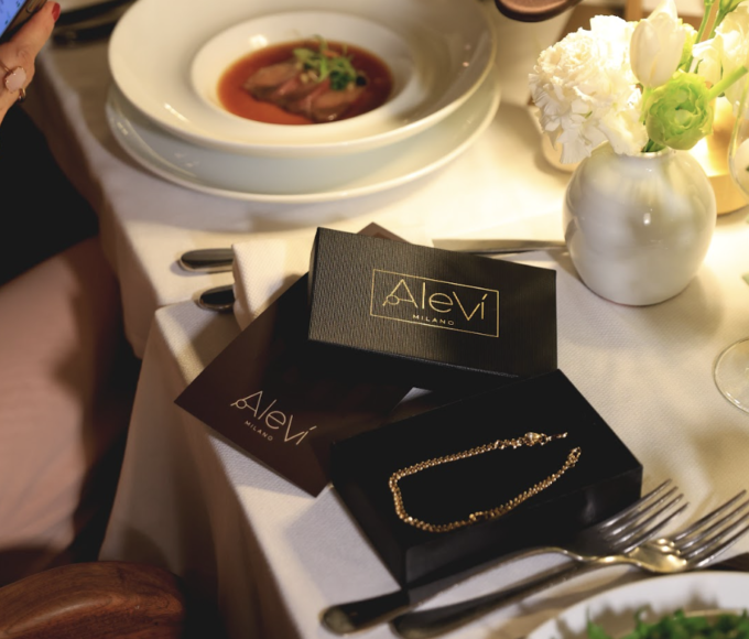 Grupo de invitadas elegantes en negro y nude alrededor de una mesa con velas en la cena de Aleví Milano FW26/27 en Blanco Castelar.