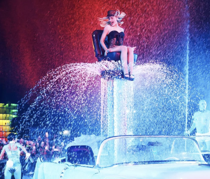 Sabrina Carpenter en el escenario principal de Coachella 2026, luciendo un minivestido Dior con flecos y brillo retro, rodeada de pantallas LED con efectos Hollywood, luces estroboscópicas y 100k fans eufóricos alzando celulares durante su hit "Espresso", capturando el vibe cinematográfico de su show histórico.