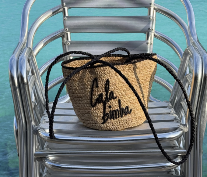 Modelos en una cala mediterránea luciendo prendas fluidas, tejidos naturales y accesorios de rafia de la colección CALA BIMBA de BIMBA Y LOLA , inspirada en la esencia relajada del verano.