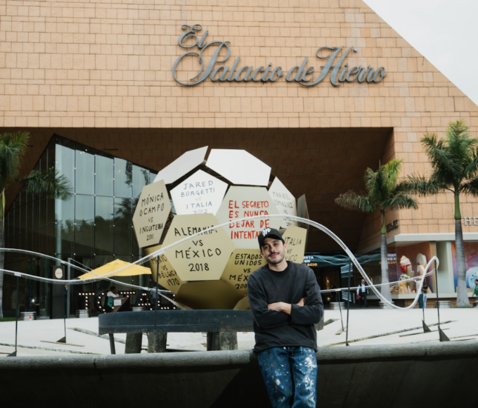 Román de Castro posa junto a su intervención artística para La Fiesta Está en El Palacio, una obra monumental inspirada en un balón de fútbol que reflexiona sobre la perseverancia y la memoria colectiva.