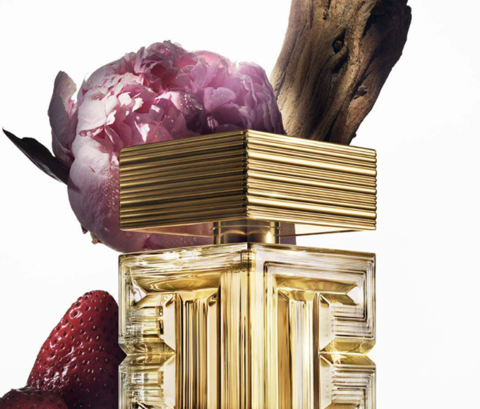 Frasco de Destin de Balmain, una fragancia floral-frutal de lujo, presentado en un diseño cúbico de vidrio transparente con detalles dorados y el icónico motivo de laberinto de Balmain.